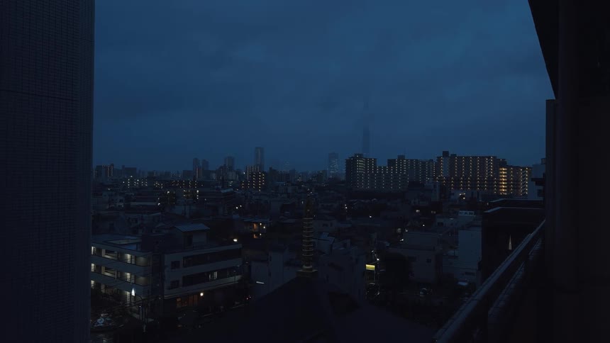 A moody view of the Tokyo city skyline with the Skytree in the distance as rain falls during a dark twilight