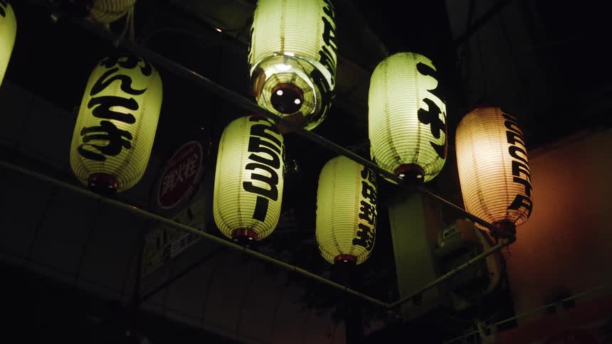 A low-angle view of illuminated Japanese paper lanterns with calligraphy glowing in a dark alley at night