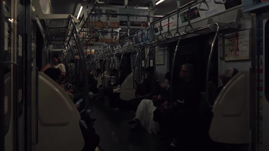 A static shot of passengers commuting on a dimly lit train at night in Japan