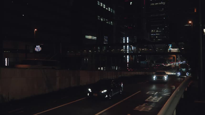 A slow stream of traffic with bright headlights cuts through the darkness of a modern city at night