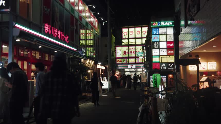 Pedestrians walk down a vibrant alley in a Japanese city at night, illuminated by colorful neon and storefront signs
