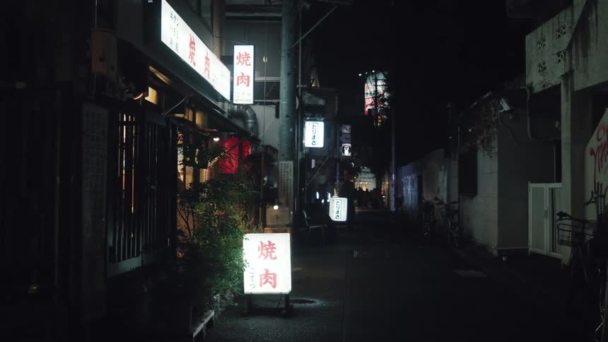 Glowing restaurant signs illuminate a quiet back alley in a Japanese city late at night