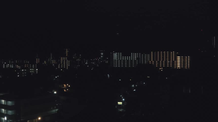 A static shot of a quiet city skyline at night, with lights blinking on and off in distant apartment buildings