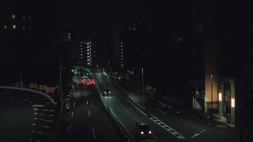 A high-angle view captures cars with headlights on traveling along a dark city highway at night
