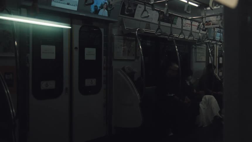 The dark interior of a moving subway train car is illuminated by flickering lights over anonymous passengers
