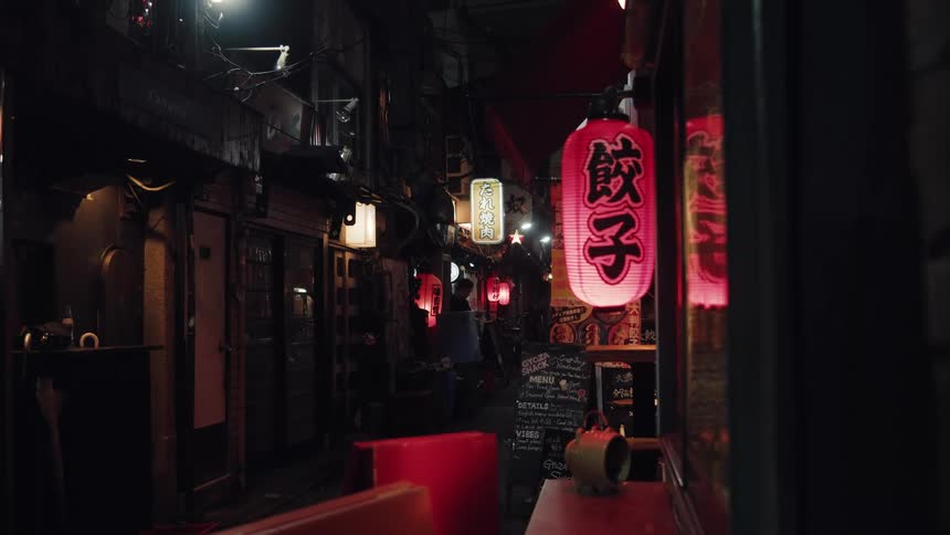 A glowing red Japanese lantern illuminates a narrow, atmospheric city alleyway in Japan at night
