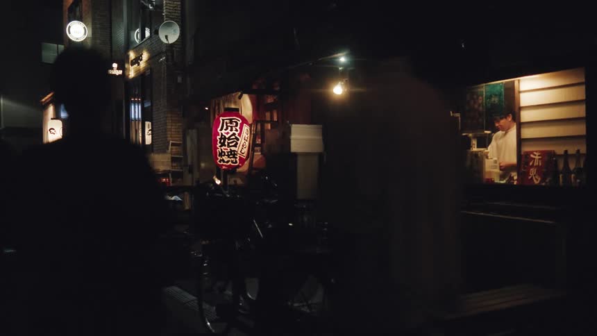 A quiet Japanese back alley at night shows a chef working inside a warmly lit restaurant as people walk by