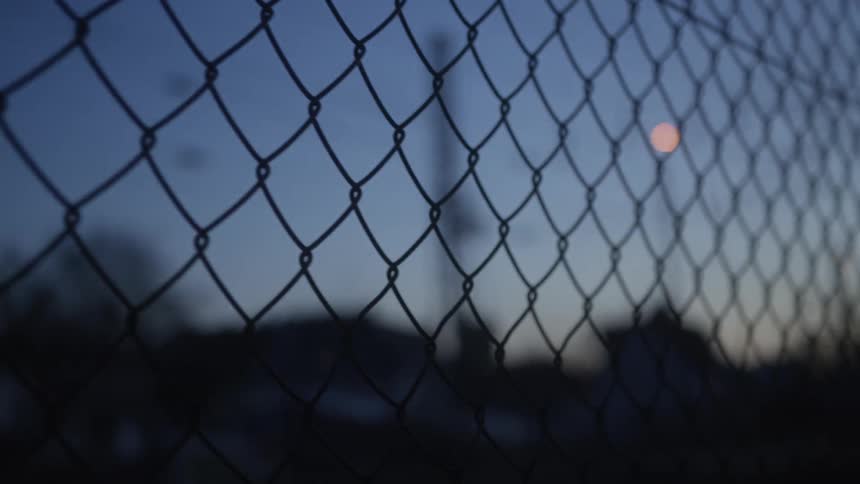 A shallow focus close-up of a chain-link fence silhouetted against a deep blue twilight sky