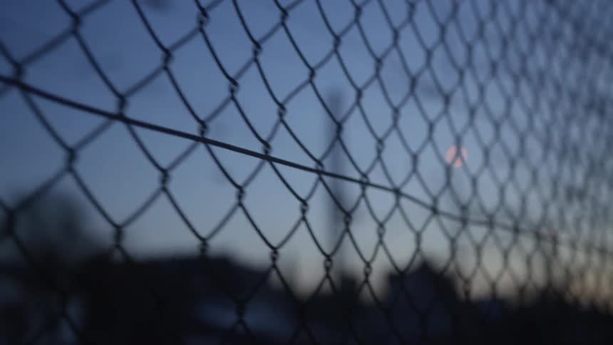 A slow pan across a silhouetted chain-link fence during a moody twilight