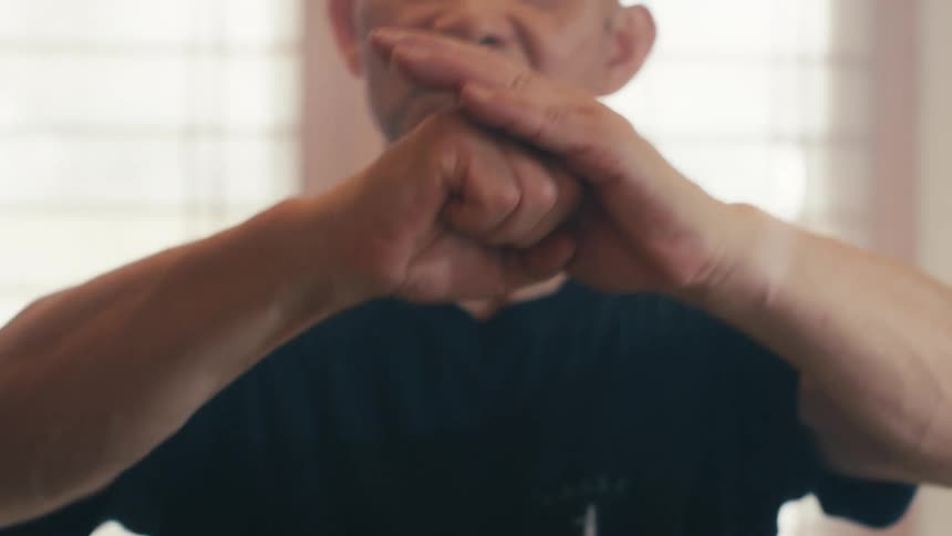 A focused older man performs a traditional martial arts kata with slow, deliberate hand movements