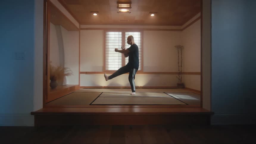 A martial artist practices his forms with slow and controlled movements in a traditional Japanese-style dojo