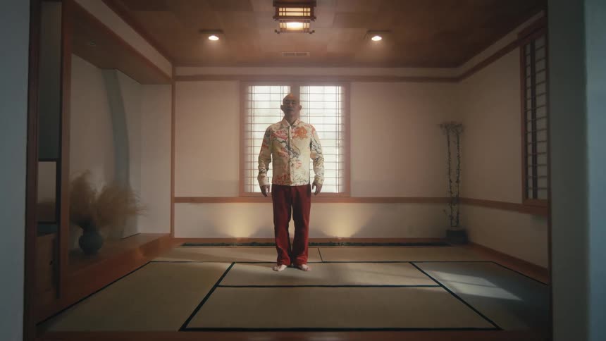 Slow push-in shot of a man standing still and centered in a tranquil, minimalist Japanese dojo
