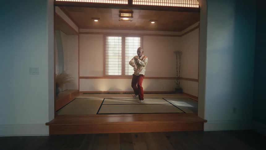 A man gracefully practices the slow, deliberate movements of Tai Chi in a serene, traditional Japanese-style dojo