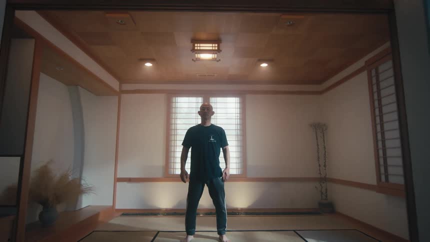 Slow pull back of a man standing stoically in the center of a traditional Japanese dojo