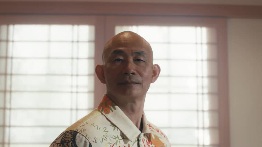 Portrait of a serene, bald senior Asian man looking at the camera inside a traditional Japanese home