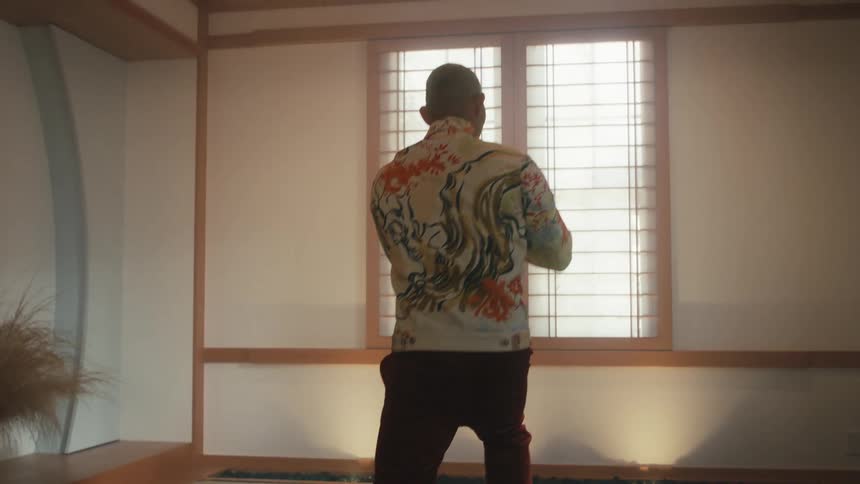 An elderly Japanese man gracefully practices a slow martial arts routine in a tranquil dojo