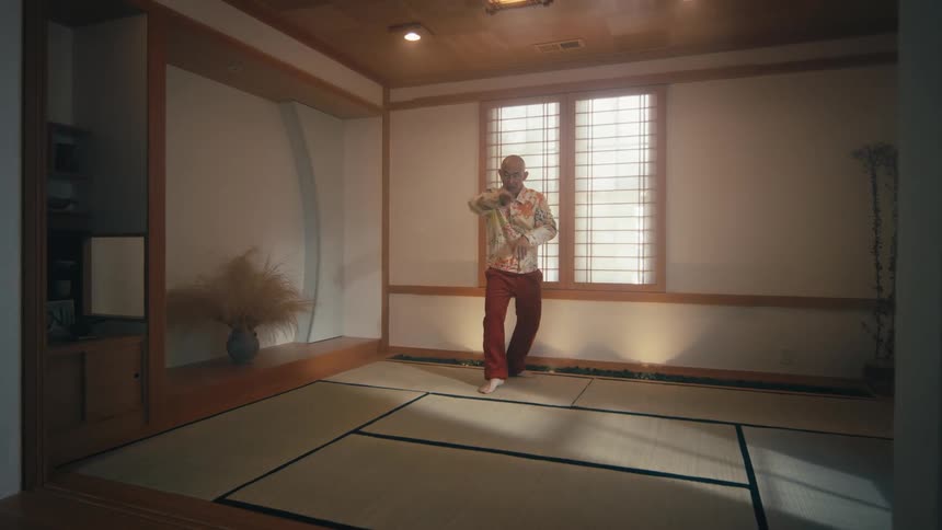 An elderly Asian man practices a slow, graceful martial arts routine in a traditional Japanese-style room