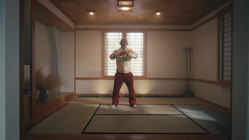 A man performs slow, meditative Tai Chi movements in a traditional Japanese dojo as the camera slowly pulls back
