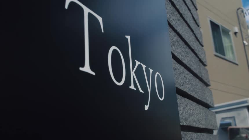 A low-angle close-up shot of a modern black sign with the word 'Tokyo' on an urban building