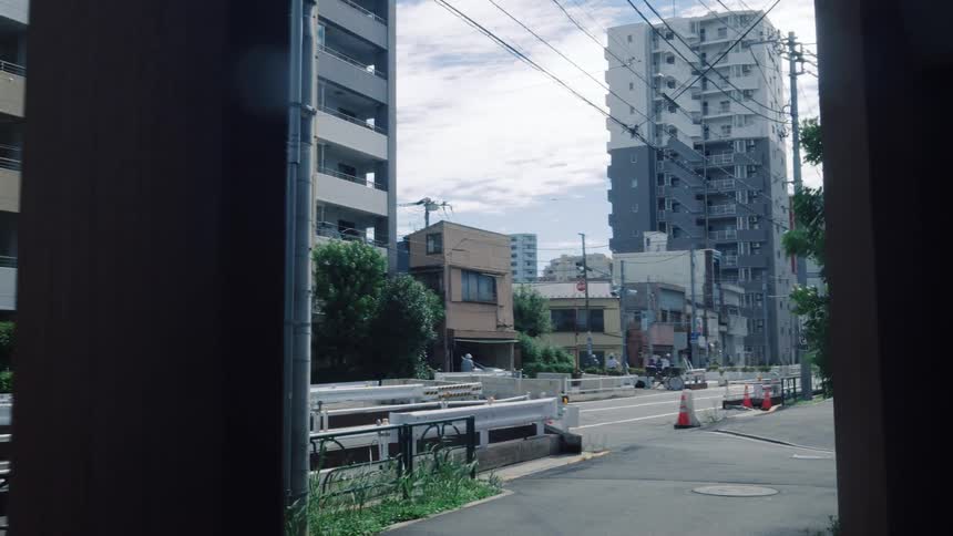 A slow dolly shot reveals a quiet, modern residential street in Japan during the daytime