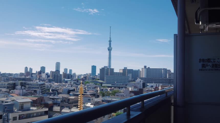 A scenic view from a balcony shows the Tokyo cityscape and the famous Skytree under a clear blue sky