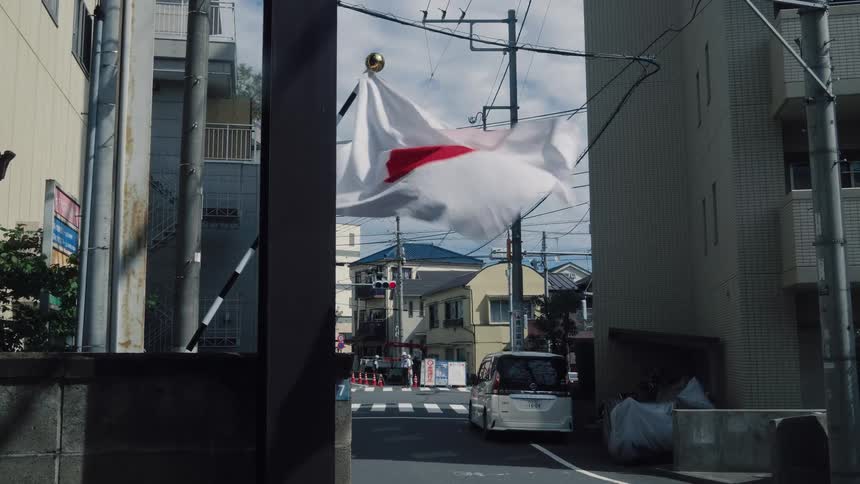 The national flag of Japan billows in the wind on a city street in slow motion