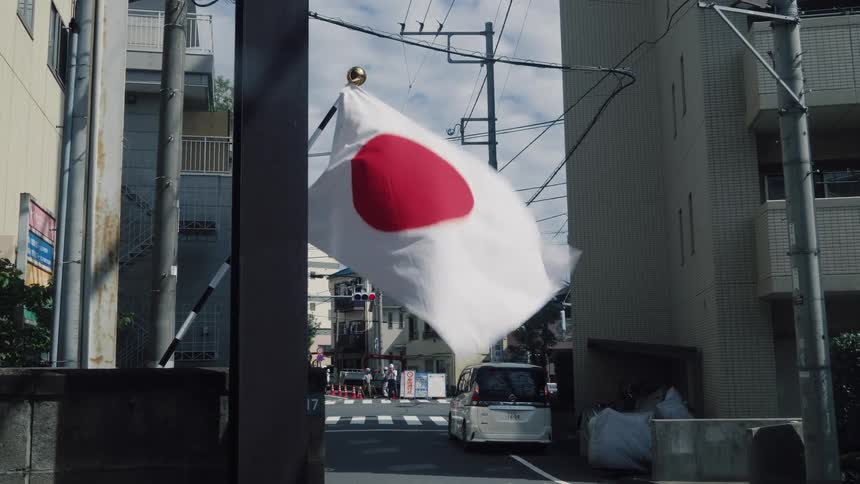 A Japanese flag waves in slow motion on a quiet residential street in a city in Japan