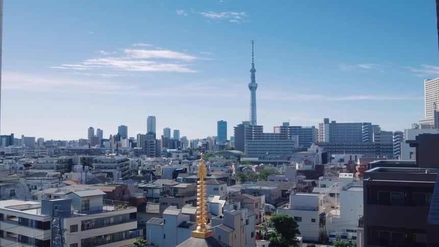 A static wide shot shows the Tokyo Skytree towering over the city's architecture on a sunny day