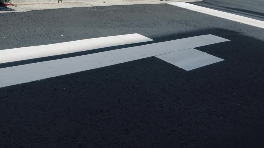 A slow zoom out reveals the white lines of a crosswalk on dark asphalt pavement in the bright sunlight