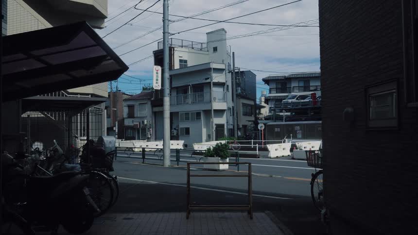 A quiet, moody shot of a Japanese residential street as a person on a bicycle and a car drive by