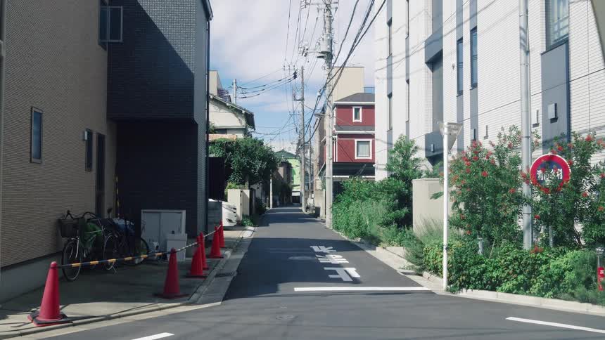 A quiet residential alleyway in a modern Japanese neighborhood on a sunny day with a cyclist passing by