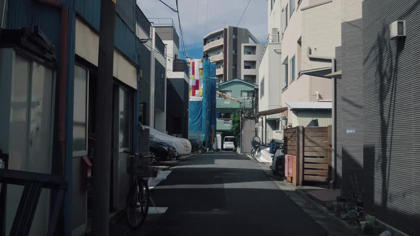Sunlight and shadows move across a quiet, narrow residential alley in urban Japan