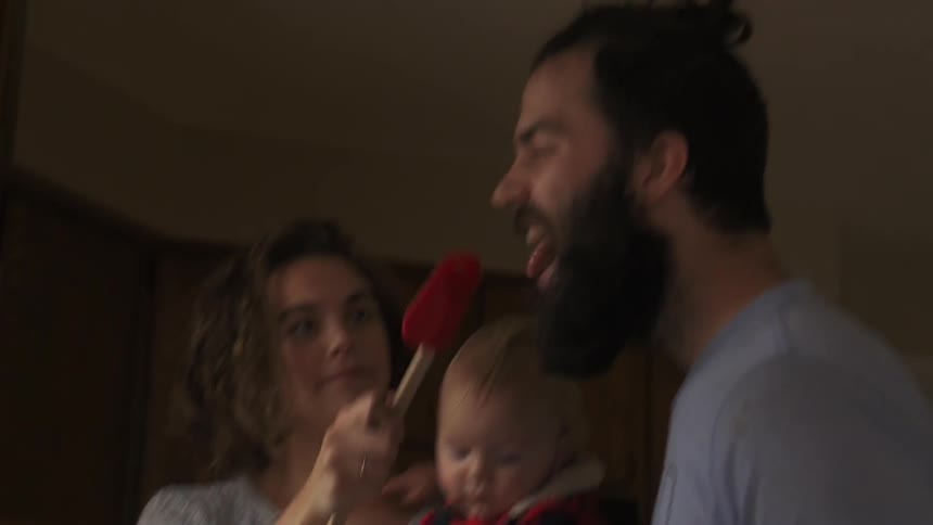 Woman holding a baby smears frosting on man's nose with spatula
