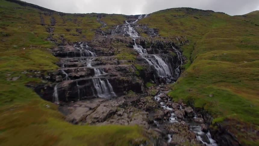 A stream flows over rocks and cliffs in a hilly area
