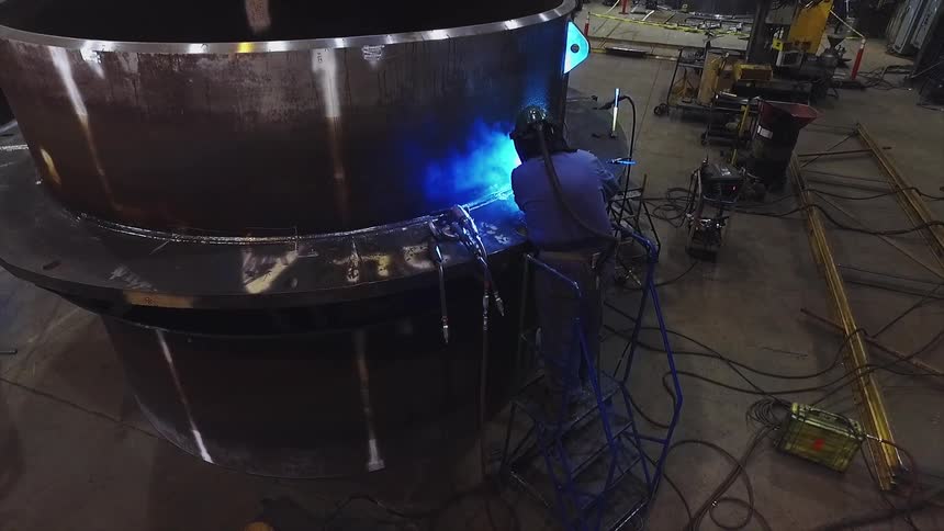 A man is welding metal in a large warehouse