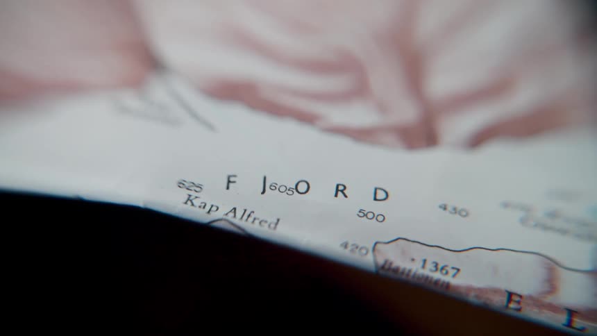 A still, extreme close-up shot focuses on the word "Fjord" on a topographical paper map