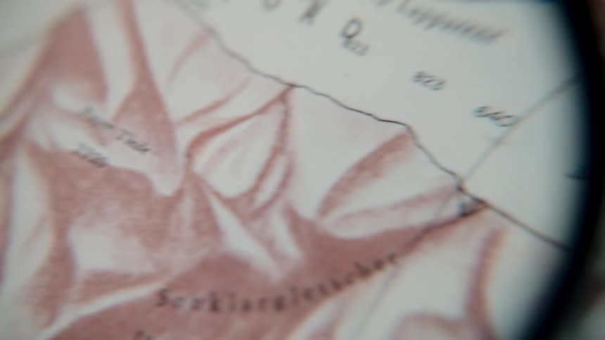 A close-up view through a magnifying glass explores the details of a vintage topographical map of a mountainous region