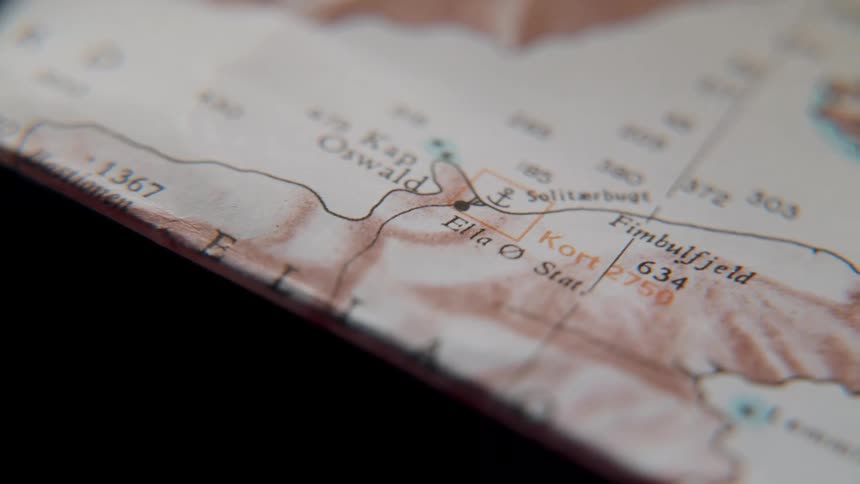 A magnifying glass moves slowly over a vintage geographical map, focusing on expedition routes and locations