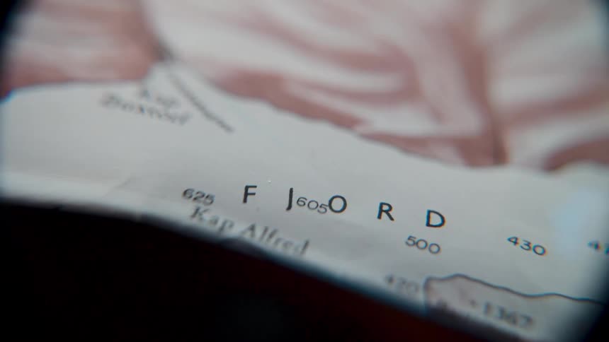 A magnifying glass is used to examine an old geographical map, focusing on the location of a fjord