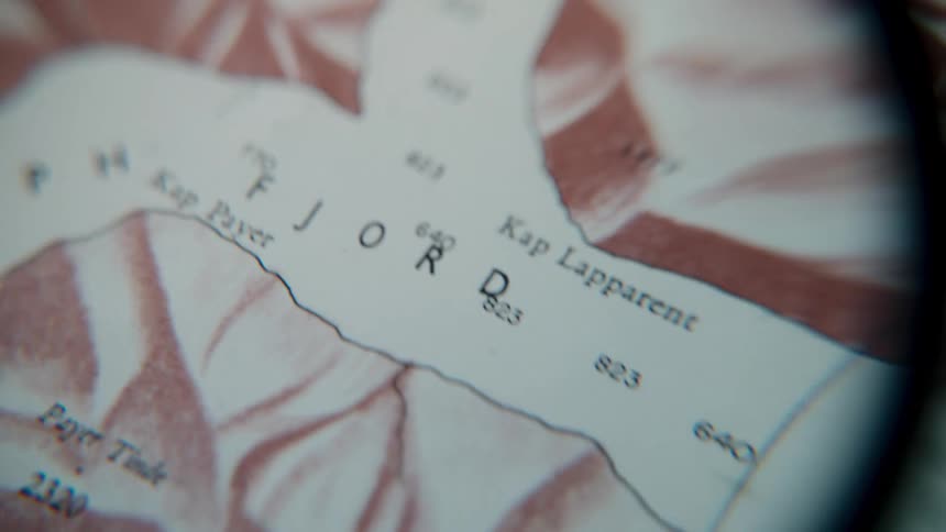 A macro lens slowly scans across a vintage sepia-toned topographical map, revealing intricate details of fjords and landmasses