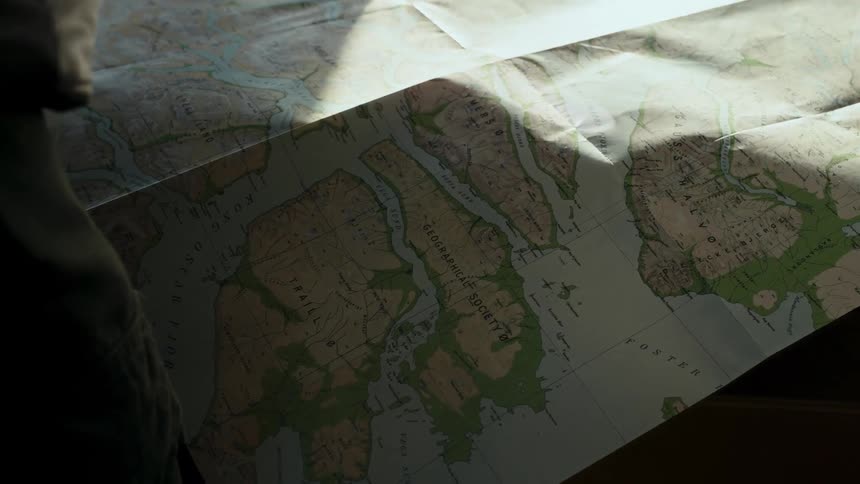Sunlight and shadows move across an explorer's geographical map spread out on a table