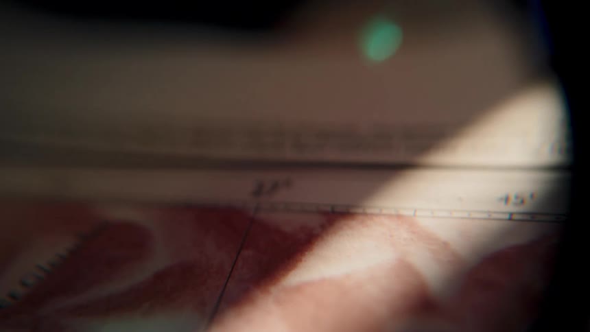 A close-up view through a magnifying glass scans across a vintage map, illuminated by a moving beam of light