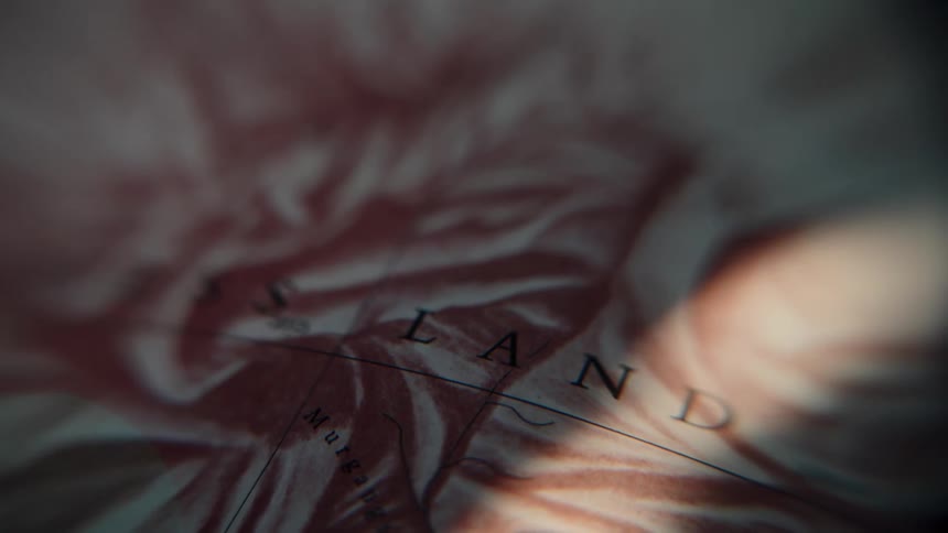 A dramatic close-up of a beam of light moving across the word 'LAND' on a vintage topographical map