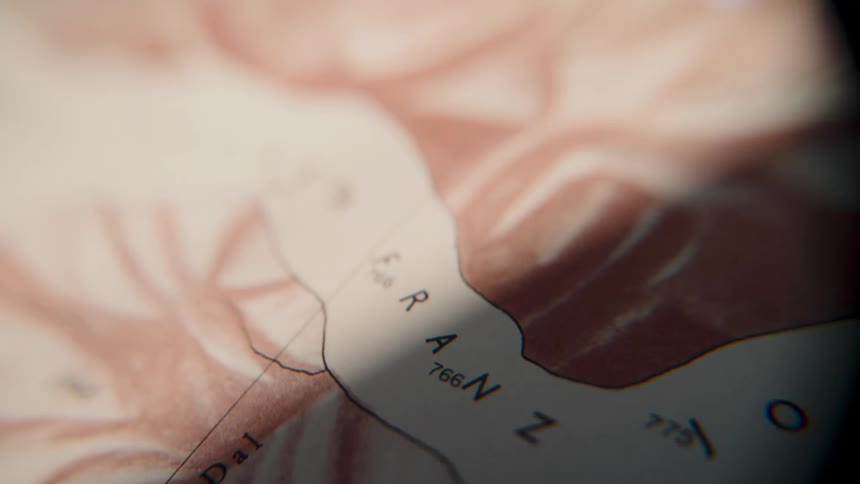 An extreme close-up view through a lens scans across a vintage topographical map with moving light and shadow