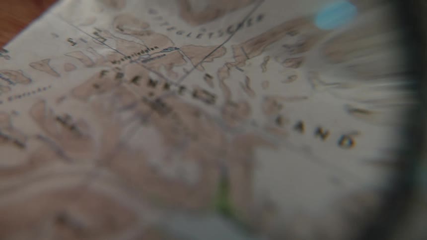 A magnifying glass scans across a vintage topographical map, exploring fjords and mountainous terrain