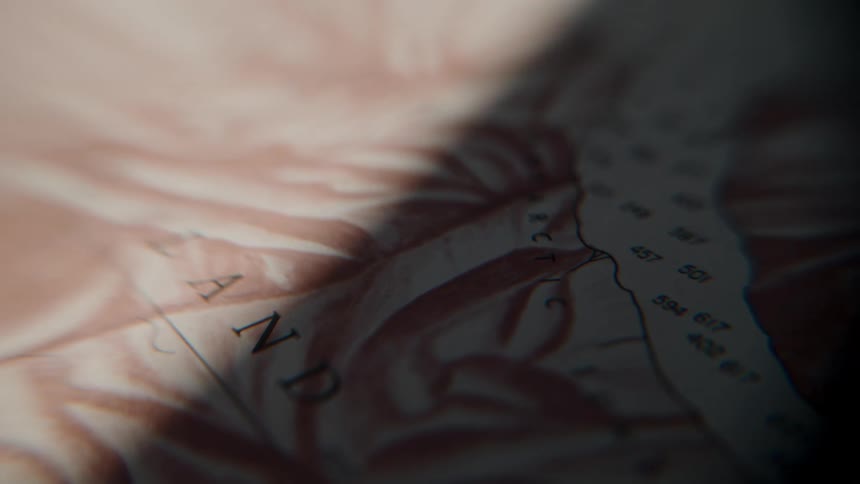 An extreme close-up of a vintage nautical map as a shadow slowly moves across the paper