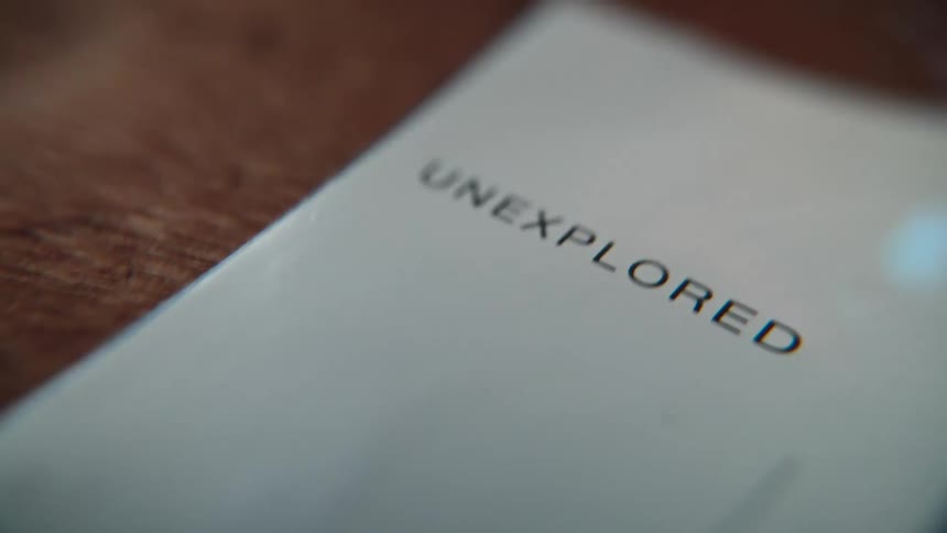 A magnifying glass inspects the word 'unexplored' printed on a piece of paper