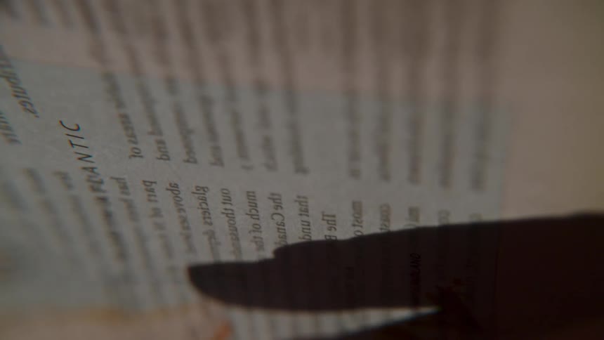 A close-up shot captures fingers tracing words in an atlas, with a shadow following along the page before it's turned