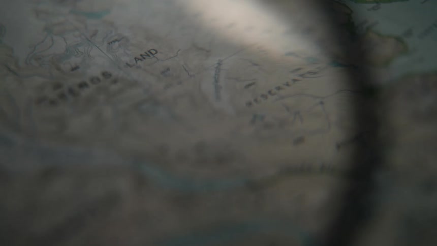 A magnifying glass slowly scans across a vintage fantasy map, searching for a destination for an epic adventure