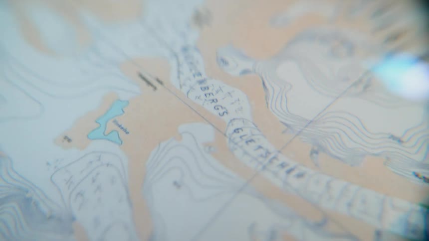A close-up, slow pan across a detailed topographic map highlighting glaciers and elevation contours